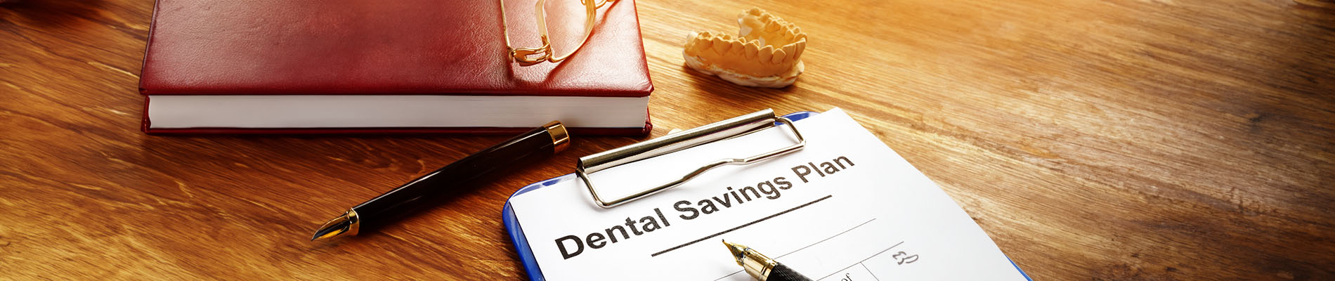 A desk with a notebook, pen, and clipboard displaying a dental savings plan.