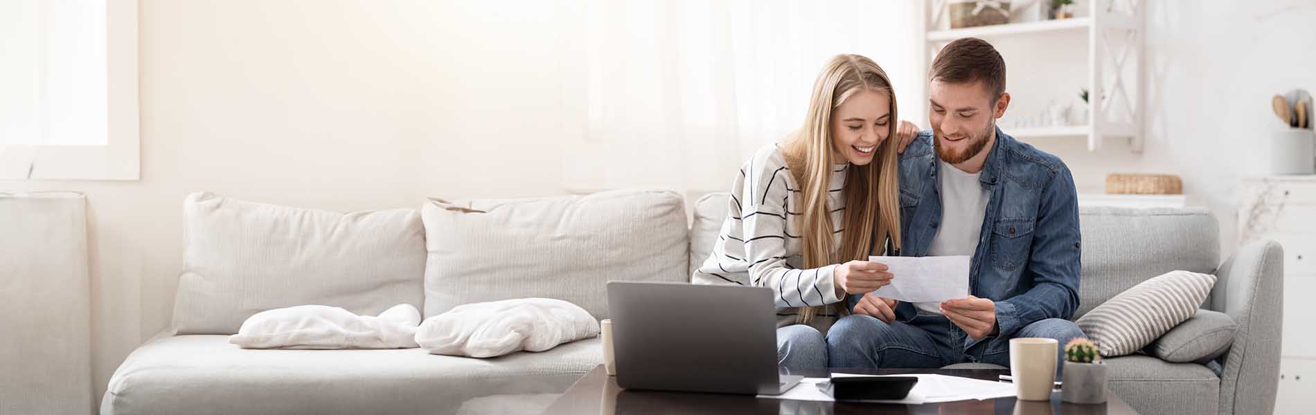 A couple sitting on a couch, engaged in reading a document together.