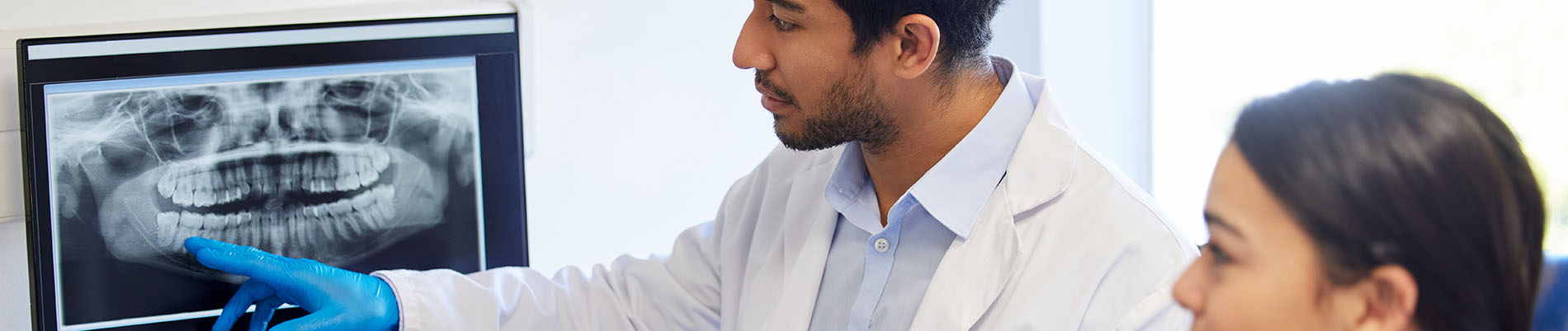 The image shows a dental professional, possibly a dentist or oral surgeon, examining an X-ray of a human skull with a patient.