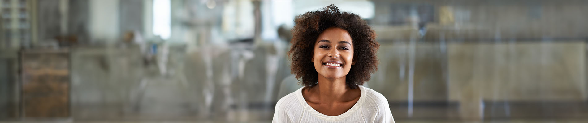 A woman with a smile, standing in front of a blurred background that suggests an indoor setting.