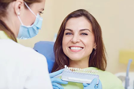 In the image, a woman is seated in a dental chair with her mouth open, receiving dental care from a professional who appears to be a dentist.