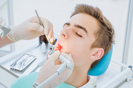 An image of a dental professional performing oral surgery on a patient, with the patient seated in a dental chair and receiving care.