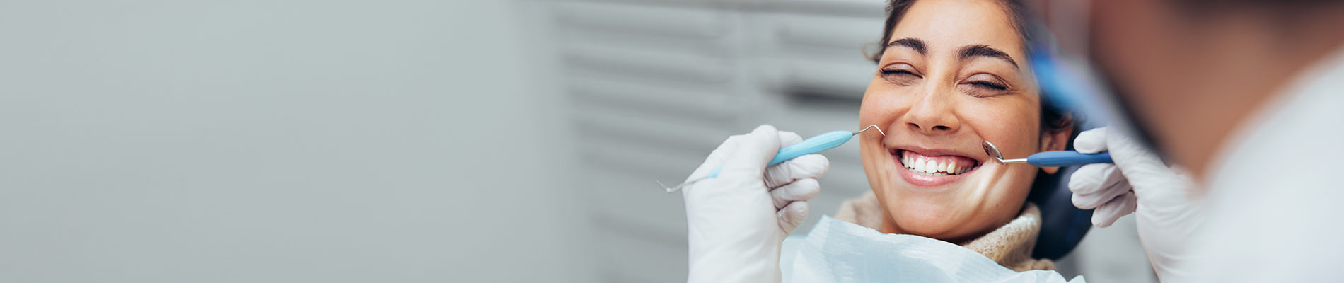 The image shows a dental professional at work, with a patient seated in the chair and smiling towards the camera.