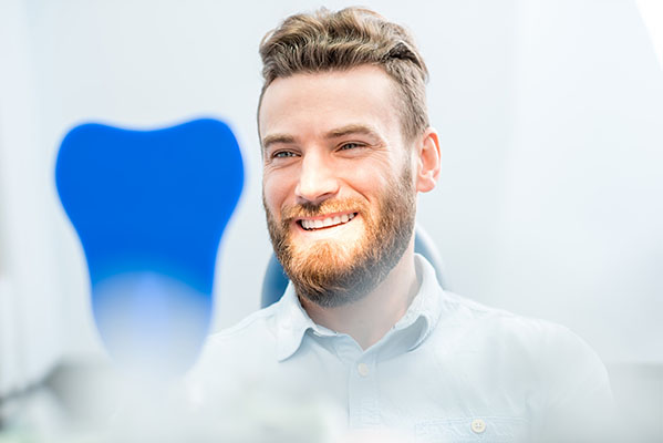 The image shows a man in a dental office, smiling at the camera, with a dental model prominently displayed behind him.