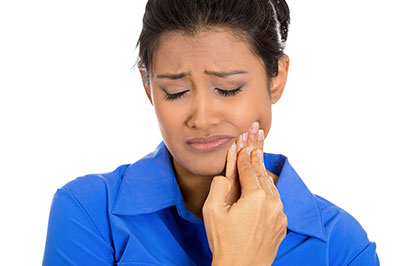 A woman in a blue shirt is intently looking at her hand, which she s holding up to her face.