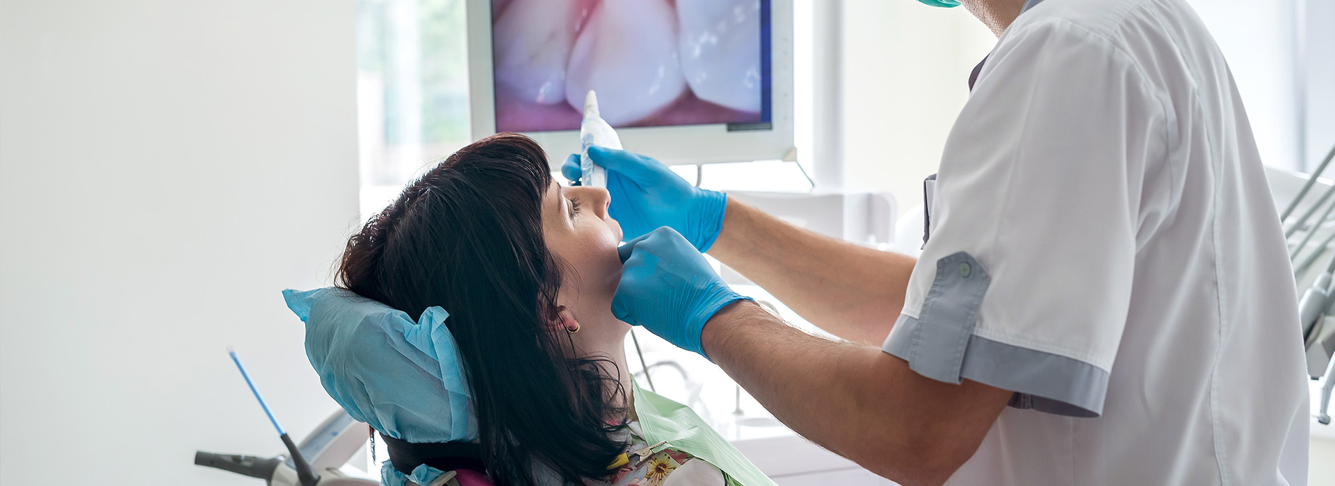 A dental professional is performing a procedure on a patient, with the patient wearing blue protective eyewear.