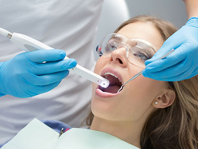 A woman in a dental chair receiving a teeth cleaning procedure with a dental hygienist using an electric toothbrush.