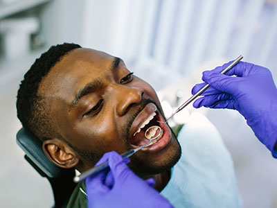 A person receiving dental treatment, with a dentist performing the procedure and using tools visible in their hands.